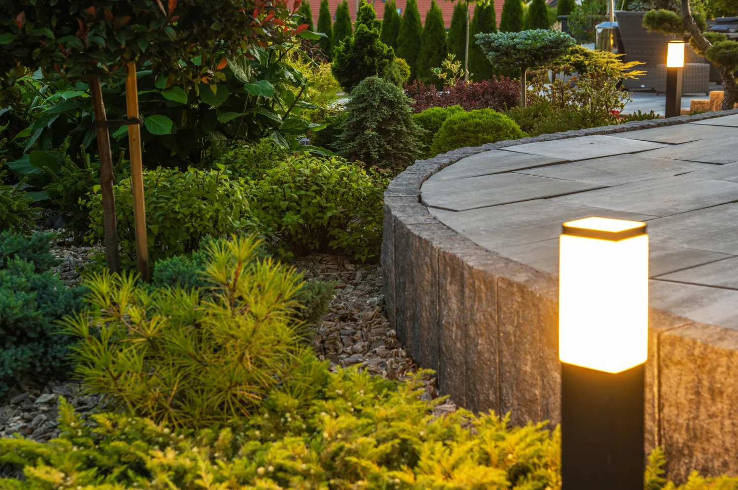 Outdoor landscape bollard light beside a stone walkway and planted bed